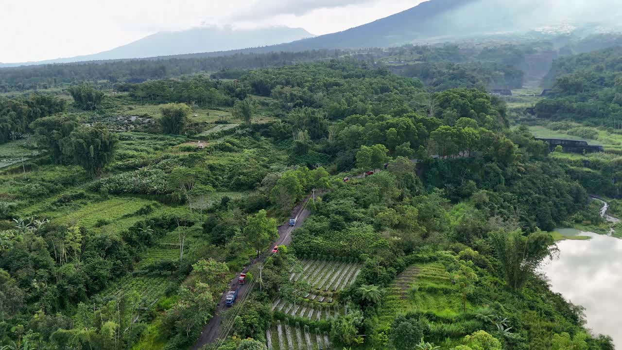 Aerial view of mining trucks driving through the green vegetation of forests and grasslands.