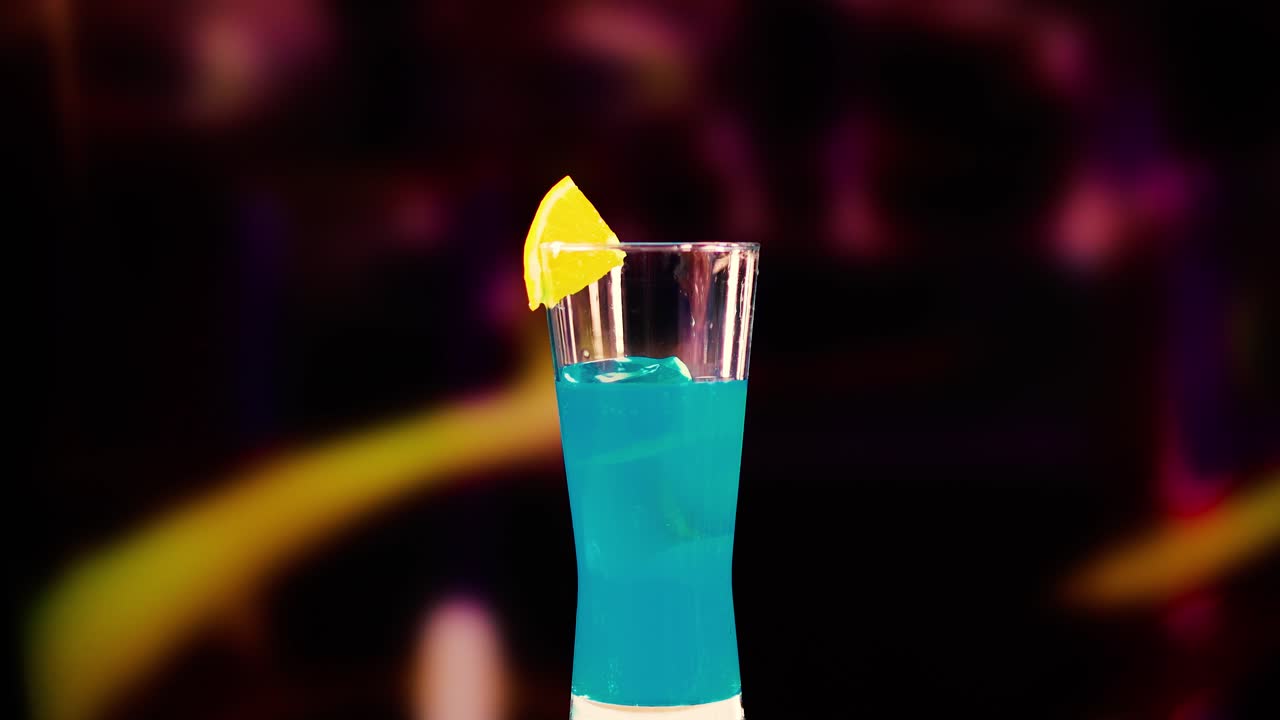 A Blue Lagoon cocktail with lemon garnish in a lively bar environment, featuring dynamic lighting and colorful background blur