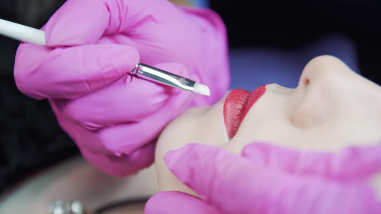 Makeup artist in pink gloves makes the lips stroke the girl. Cosmetology procedures