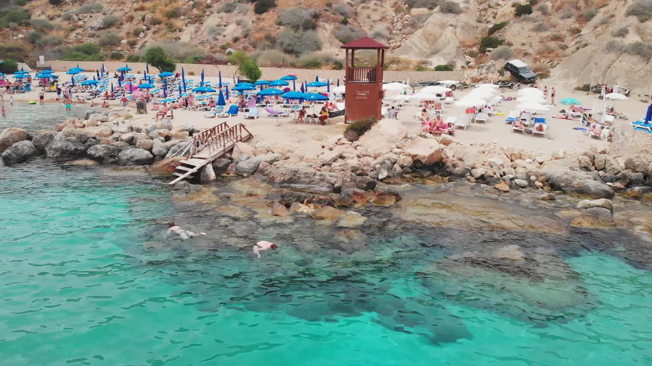 AYIA NAPA, CYPRUS - JUNE 05, 2019: Cinematic drone shot of Konnos Beach at daylight. People swimming and having fun
