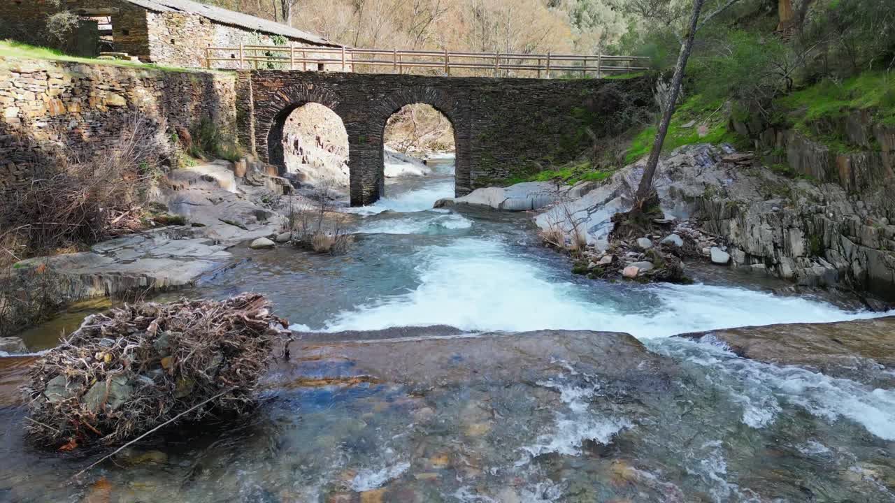 Vista de dron de un puente de piedra medieval que cruza un río de corriente rápida con un cañón rocoso y un paisaje natural en Extremadura, España. Un pintoresco destino de viaje y patrimonio europeo.