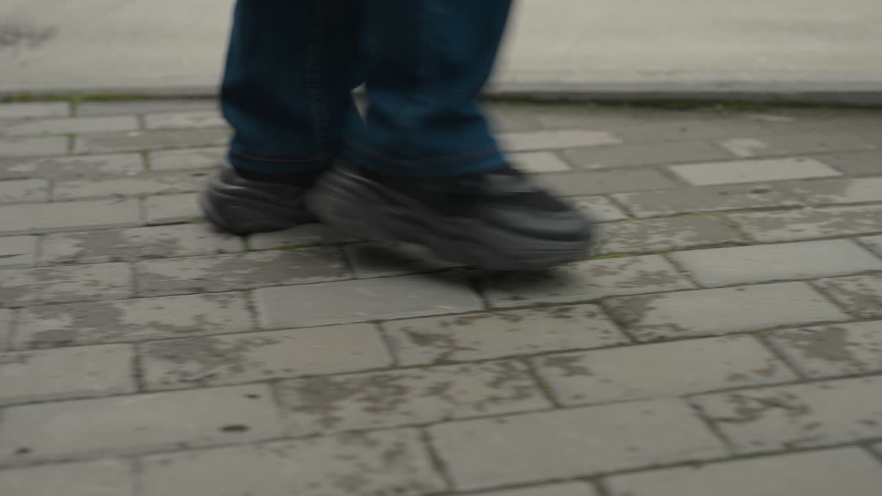 closeup walking shoes on wet pavement, steady commuter steps across brick sidewalk with small puddles, jeans and dark sneakers, lowangle framing capturing sole impact, reflective city surfaces