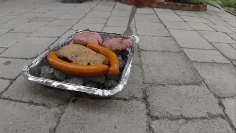 locked off view of disposable mini bbq grill with different meats