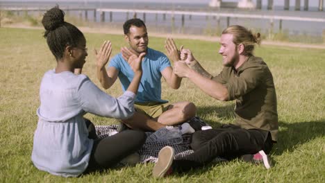 Fröhliche-Junge-Leute-Spielen,-Während-Sie-Auf-Der-Wiese-Sitzen