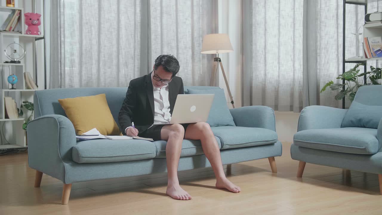 집에서 노트북으로 작업하는 동안 재과 쇼트를 입은 아시아 사업가의 전체 시각