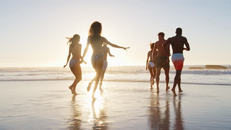 Grupo-De-Amigos-Corren-Juntos-A-Través-De-Las-Olas-En-Vacaciones-En-La-Playa