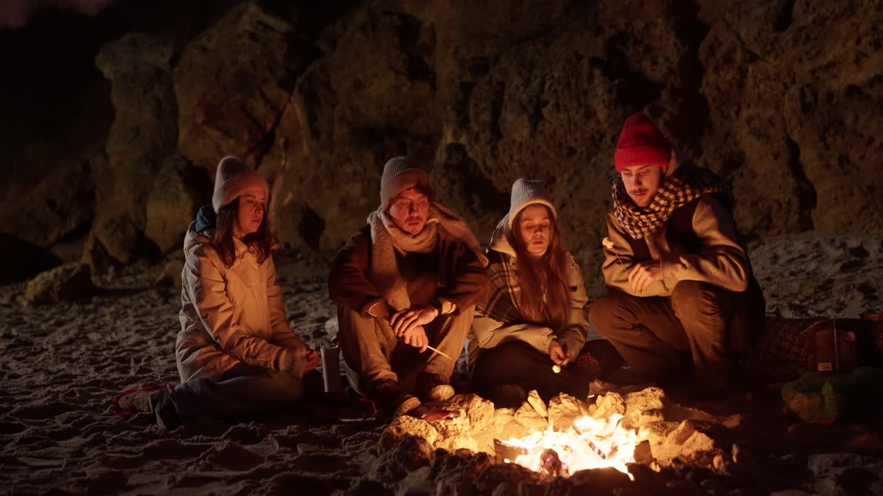 Friends roasting marshmallows by a campfire on a winter beach