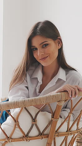 pretty positive woman artist in casual clothes rests smiling in rattan armchair with pillows near easel with picture in spacious studio slow motion