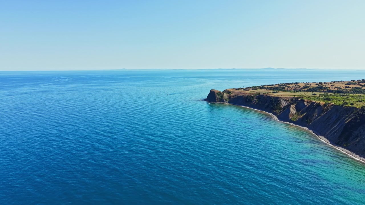Acque azzurre e luminose incontrano colline verdi sulla costa, catturando la bellezza della natura in una scena diurna soleggiata vicino alla riva.