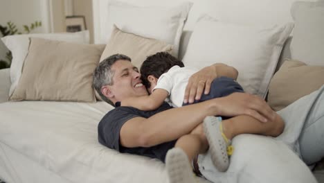 happy dad playing and romping with little son on couch