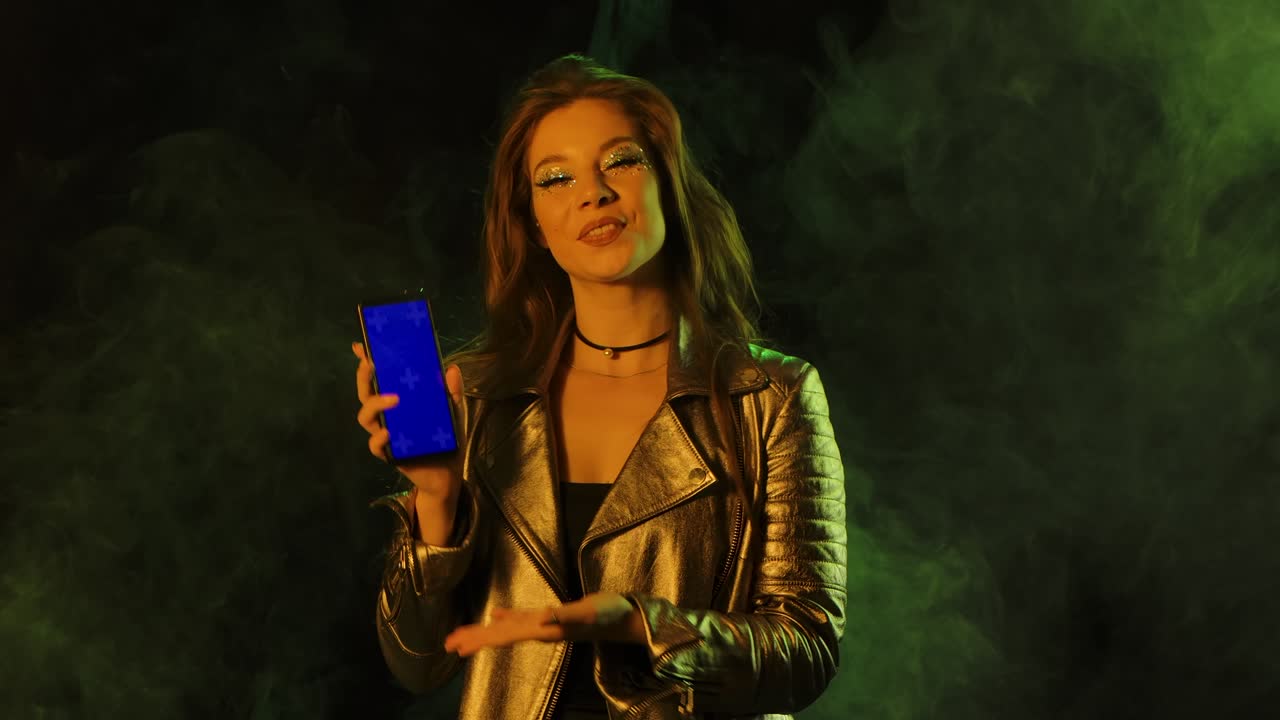 Portrait of young pretty woman is texting on her phone then shows smartphone with a blue screen chroma key and showing thumbs up gesture. Close up. Slow motion