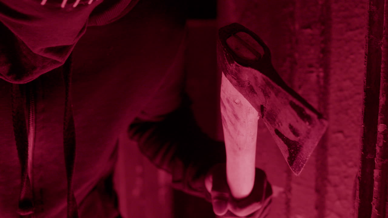 крупным планом вид на ожидающего мужчину в черной балаклаве и с топором в руках, спрятанного в разрушенном здании