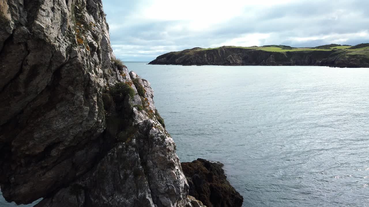 panorámica a través de la playa de traeth porth wen hasta la formación de un arco de piedra escarpada en la costa del mar de irlanda
