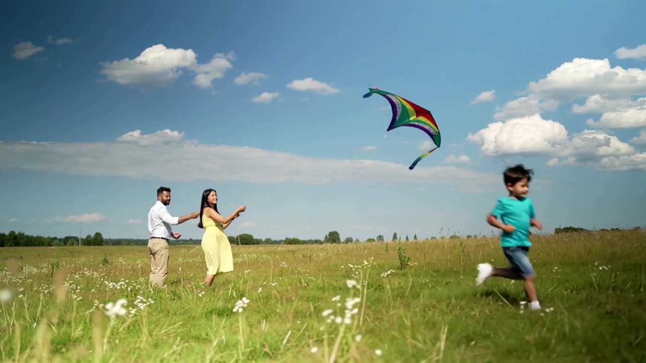 Una donna in abito giallo lancia un aquilone arcobaleno, guidando la corda mentre la brezza lo solleva attraverso il prato.