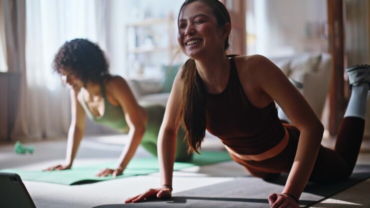 Two women doing pushups yoga mats home. Fitness training together with tablet.