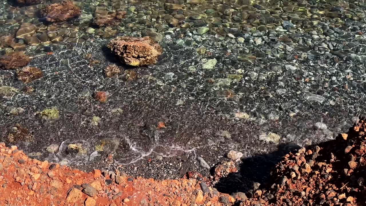 Waves washing over clear shallow water and rugged rocks on a beach in Crete Greece