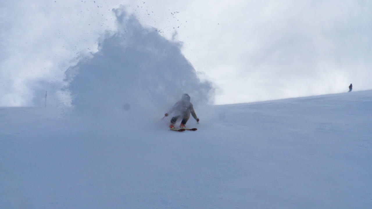 Dynamic footage of a freeride skier skiing straight toward the camera and throwing a huge snow spray. Powerful turn, deep powder, speed, and raw alpine energy in a winter mountain setting