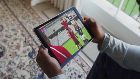 Zusammensetzung-Eines-Mannes,-Der-Zu-Hause-Sitzt-Und-Sich-Ein-Rugbyspiel-Auf-Einem-Tablet-Anschaut