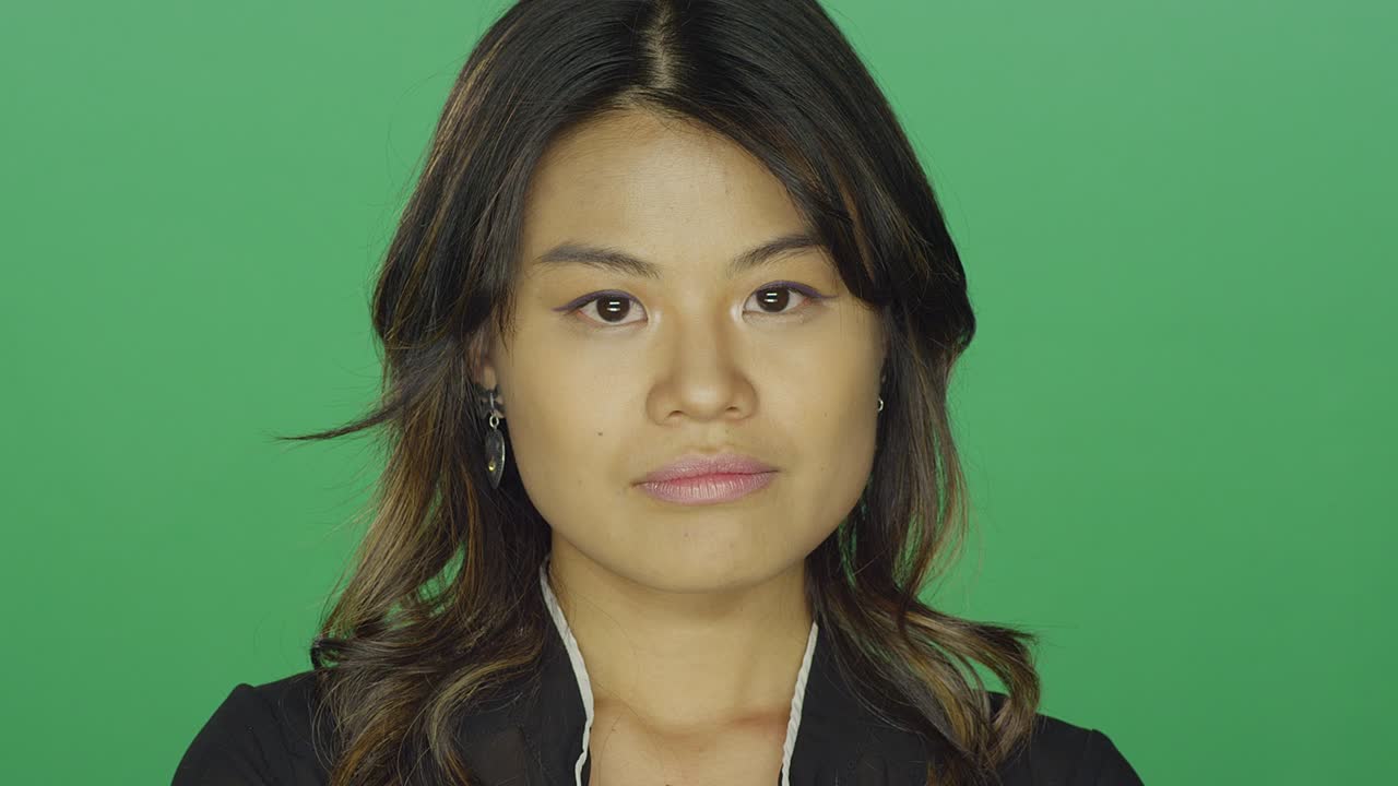 젊은 아시아 여성은 그녀의 팔을 교차하고 초록색 스크린 스튜디오 배경에서 화를 내고 있습니다.