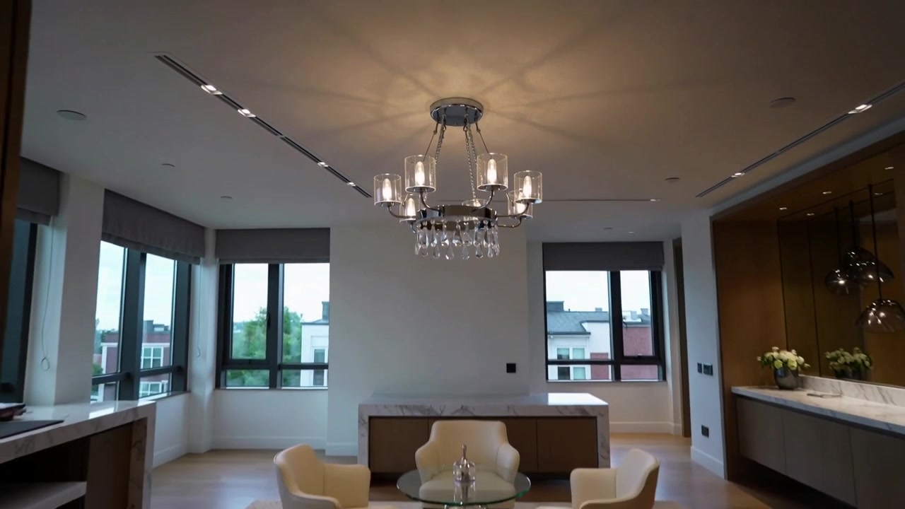 Pulling back camera revealing metal chandelier casting soft ceiling shadows over dining and kitchen