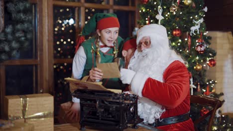 santa with two elves on christmas decorated background. old santa claus looking on different envelopes through the magnifying glass with the help of elves.