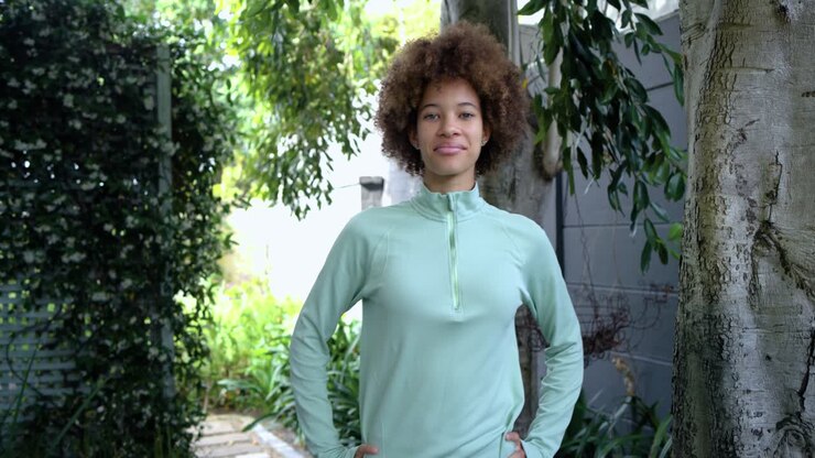 Donna afroamericana che cammina lungo un sentiero del giardino, guarda a sinistra e poi posa per la fotocamera, sorridendo