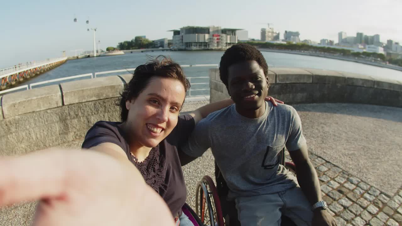 pareja alegre usando sillas de ruedas tomando video en el muelle