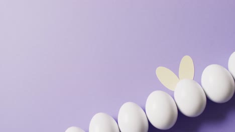 white easter eggs with rabbit ears on purple background with copy space