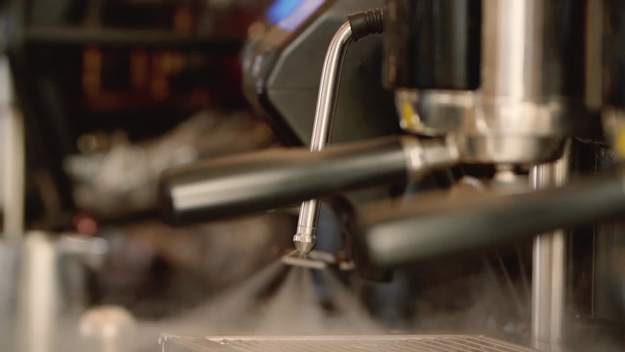 Vaporizador de cafetera liberando vapor arremolinado, destacando el arte del barista y la preparación del espresso, primer plano a cámara lenta
