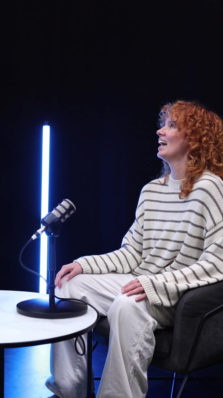 Donna dai capelli rossi che parla e gesticola durante la registrazione di un podcast.