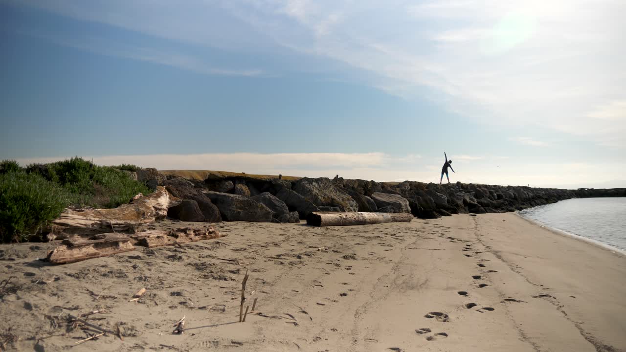 Person stretching on rocky pier by the beach on a sunny day