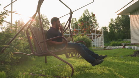 golden sun rays filter through trees onto man seated on swing bench eating handful of ripe strawberries freshly harvested from garden while relaxing in tranquil orchard setting
