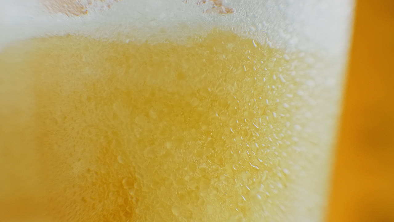 Birra che si versa in un bicchiere inclinato. IPA alla spina. Birra chiara fredda in un bicchiere con goccioline d'acqua. Birra artigianale che forma onde in primo piano. Freschezza e schiuma. Sfondo di bar. Birra artigianale di microbirrificio