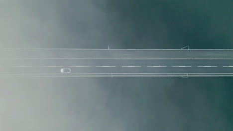 white car drives over bridge, birds eye view above clouds