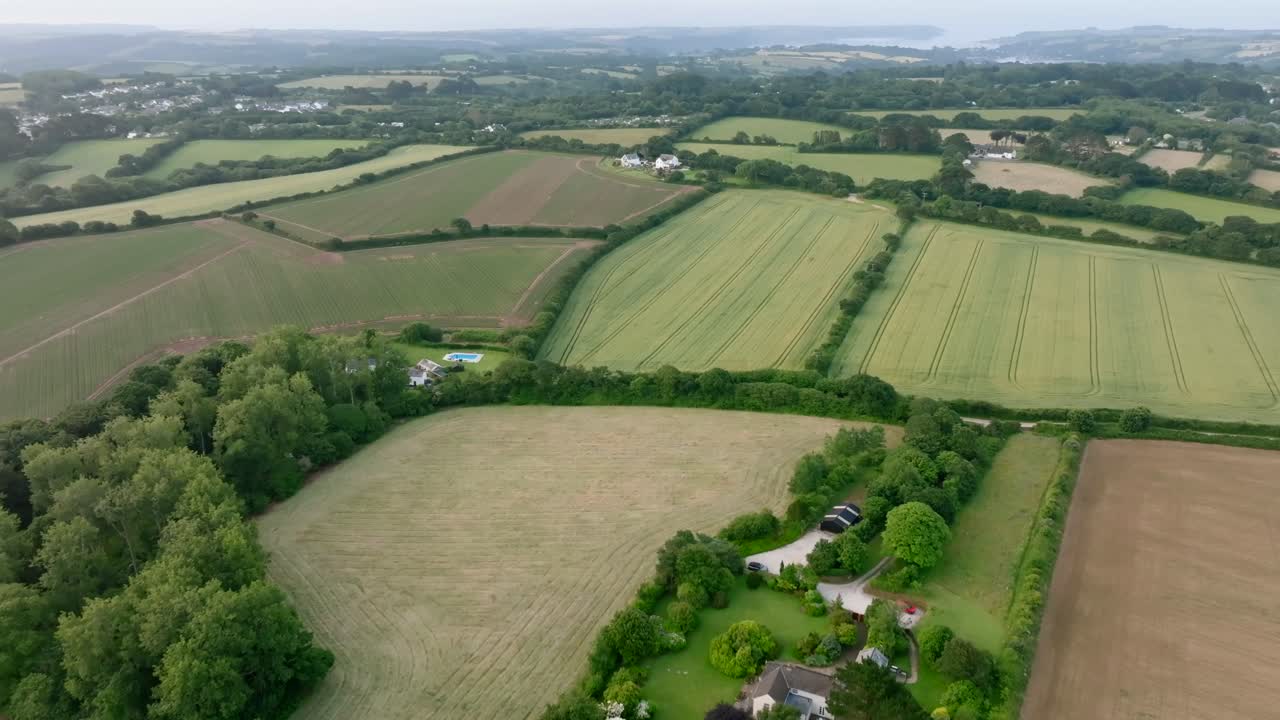 Farmhouse with immaculate garden surrounded by farmed fields lined by hedgerows and dense green woodland. Summer, Cornwall, UK.