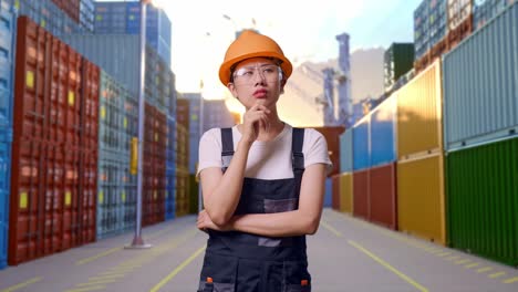 trabajadora asiática con gafas de protección y casco de seguridad pensando y mirando a su alrededor y luego levantando el dedo índice mientras estaba de pie en el almacén del patio de contenedores
