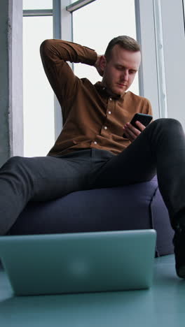 typing business message. young modern businessman using smartphone while sitting in the office vertical video