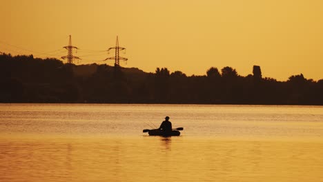 silhouette of a man floating in a boat on the river surface on the background of an evening trees. fisherman roams with oars while sailing on a row boat in the lake at beautiful sunset.