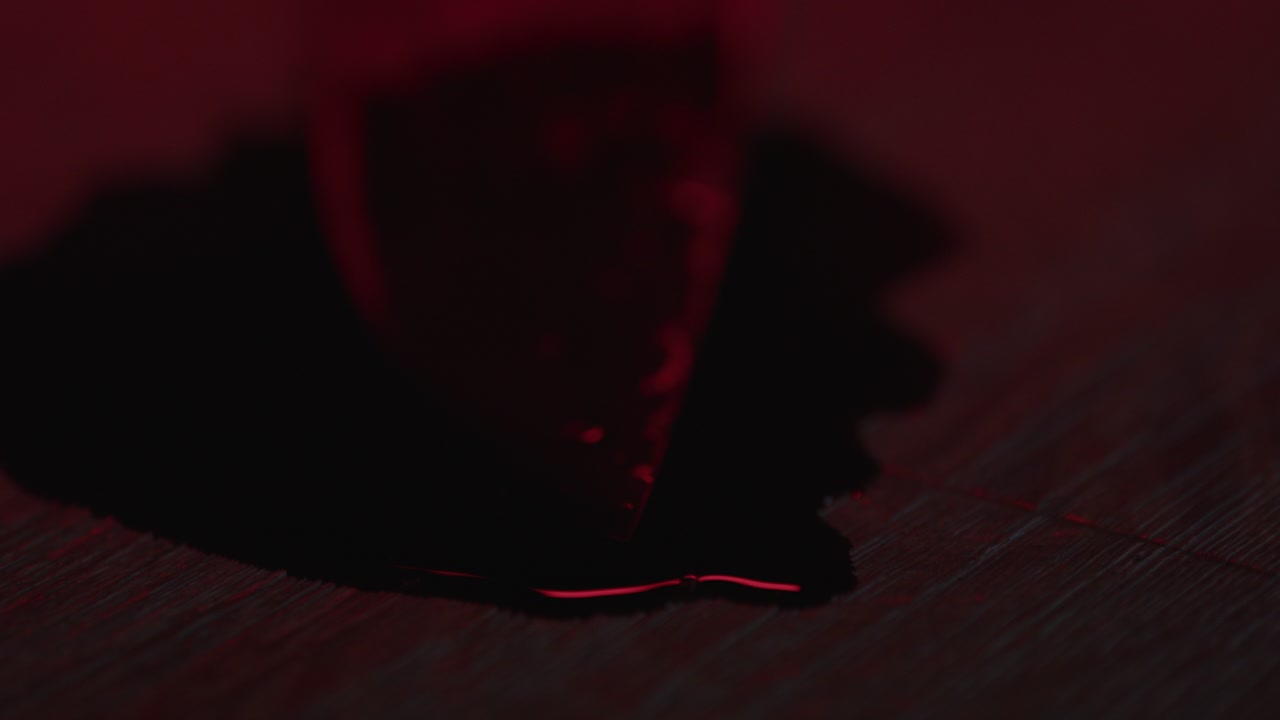 punta afilada de un cuchillo de cocina cubierta de sangre en un charco de sangre con luces de policía parpadeantes en el fondo