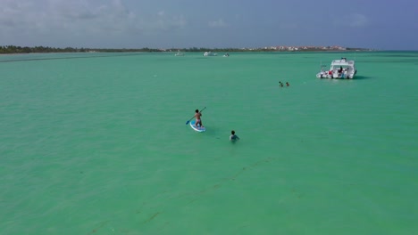 people swim and paddle-board around luxury yachts anchored in exotic tropical dominican republic ocean water, drone aerial