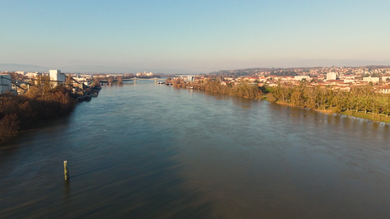 Villefranche-sur-Saone,Rhone,France flight along the majestic River Saone over the jetty towards the bridge with riverside walks and the town beyond in golden afternoon sun with clear blue sky