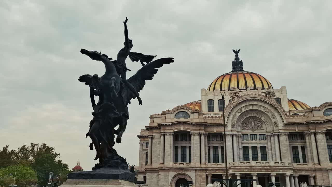 A bronze Pegasus sculpture stands in front of the Palacio de Bellas Artes, showing the building’s domed roof and ornate facade under a cloudy sky in Mexico City
