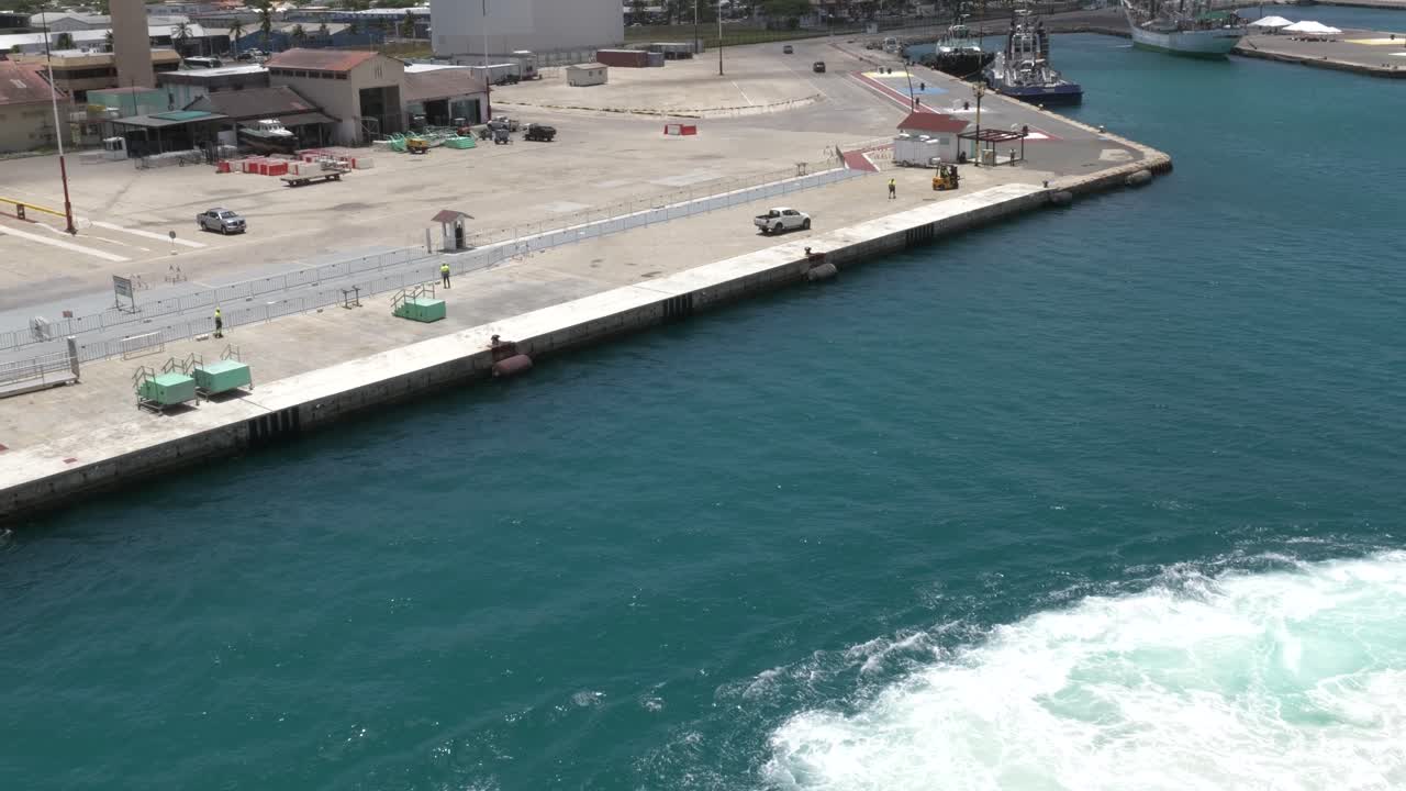 waves emanate in the turquoise blue water of the Caribbean as carnival cruise ship docks at Port of Oranjestad in Aruba viewed form cruise ship