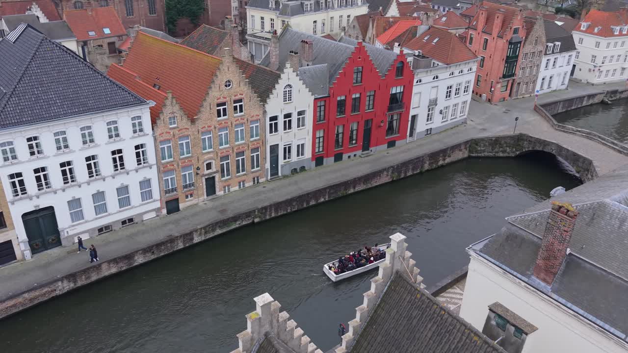 Ripresa con drone dall'alto che mostra gli iconici tetti a gradone di Bruges, Belgio. Un battello turistico scivola lungo il canale sullo sfondo, circondato dall'architettura fiamminga medievale.