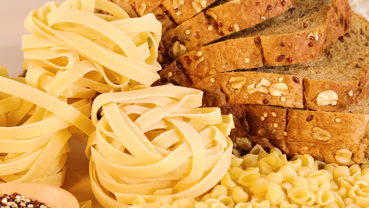 Whole wheat bread and various grains arranged with pasta under soft, warm lighting. Close-up view highlights textures and colors