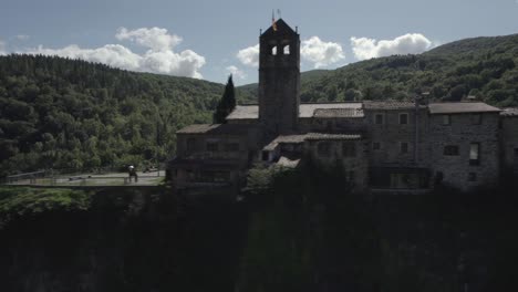 Drone's-panoramic-video-showcases-the-breathtaking-beauty-of-Castellfollit-de-la-Roca,-Spain:-medieval-village-perched-atop-a-striking-volcanic-cliff