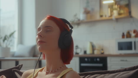 girl in headphones listening to music and singing on couch at home