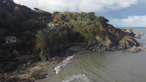 High-aerial-drone-orbit-of-houses-on-top-of-a-coastal-cliff-and-rock-formations---Lee-Bay,-Beach,-Ilfracombe,-Devon,-England