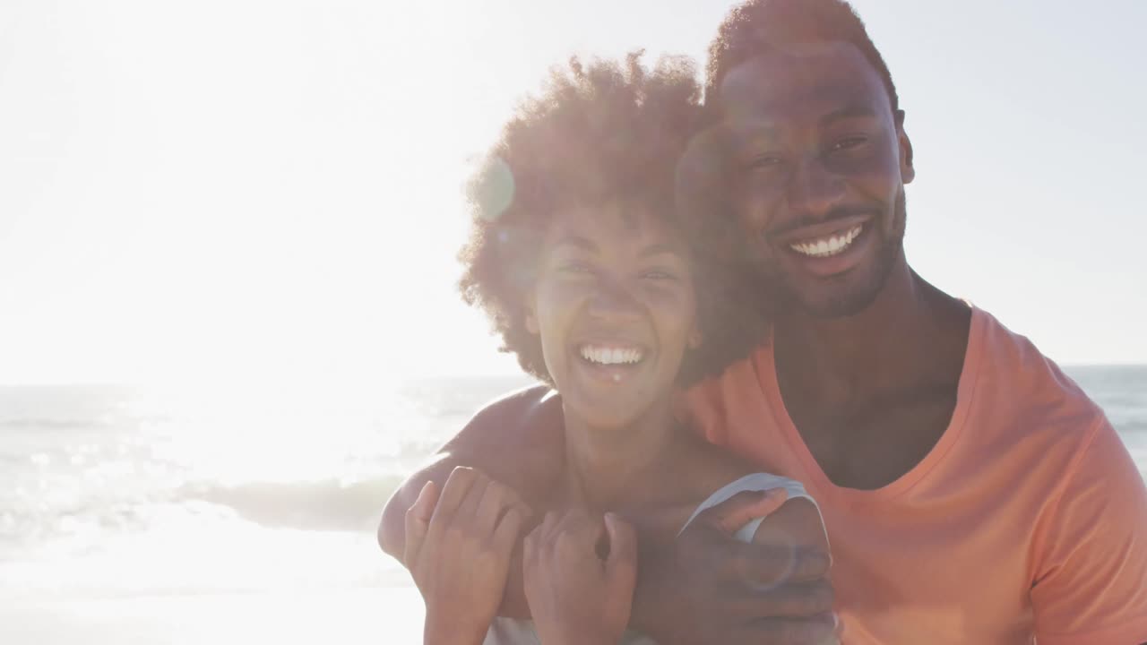 Portrait of smiling african american couple embracing on sunny beach