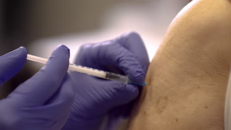 un médico con guantes de protección azul está dando la vacuna contra la enfermedad covid-19 al primer plano de la mujer madura